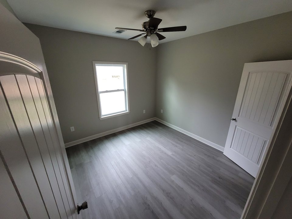 Finished room with gray wood-look flooring, white paneled doors, white trim, and a ceiling fan.