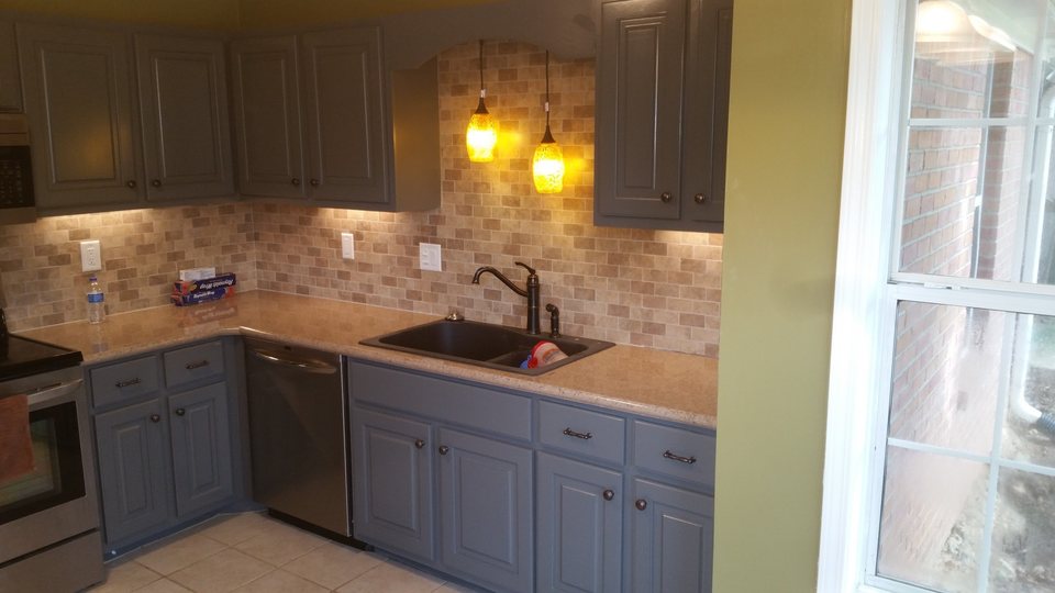 Kitchen with gray cabinetry, a tiled backsplash, warm pendant lights, and a dark sink.